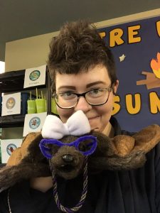 Photo of Shannon smiling and holding a bat puppet that is wearing a bow and a necklace